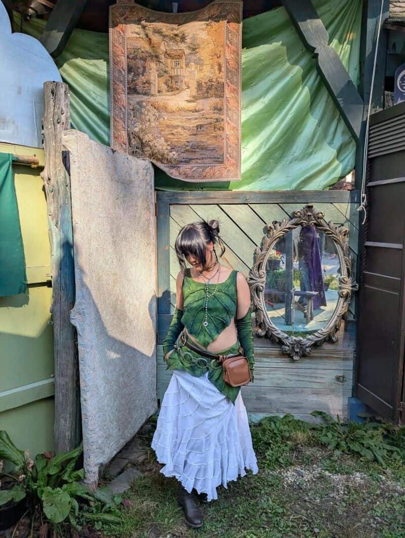 Woman in green top and white skirt at upcycling crafts market with mirror and artwork.