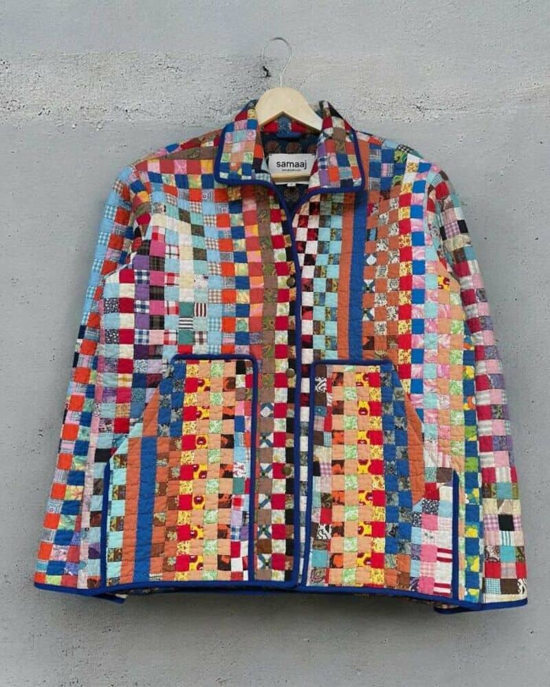 Colorful patchwork upcycled jacket on hanger against gray wall.