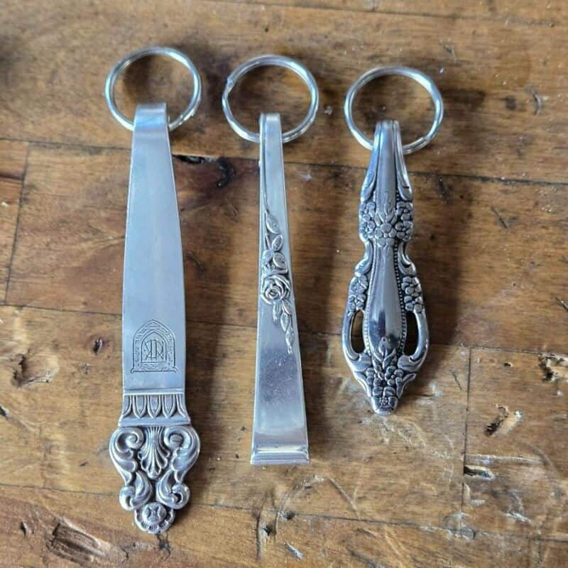 Three vintage silver keychains with ornate designs on a wooden surface.