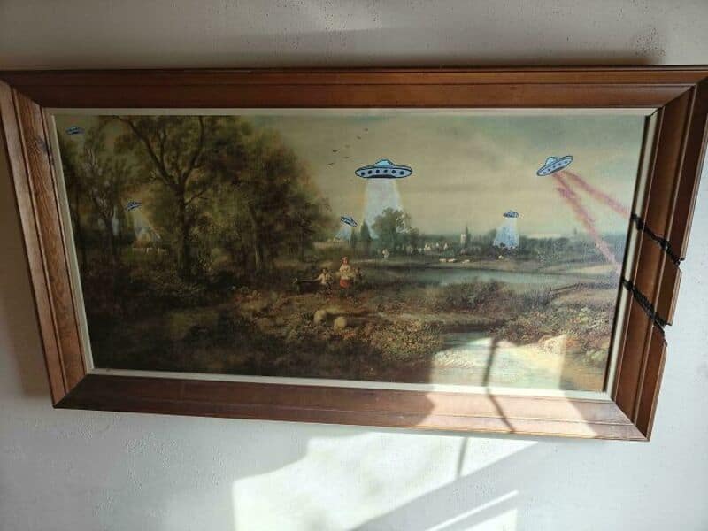 Framed landscape painting with UFOs and laser beams in a rural scene.