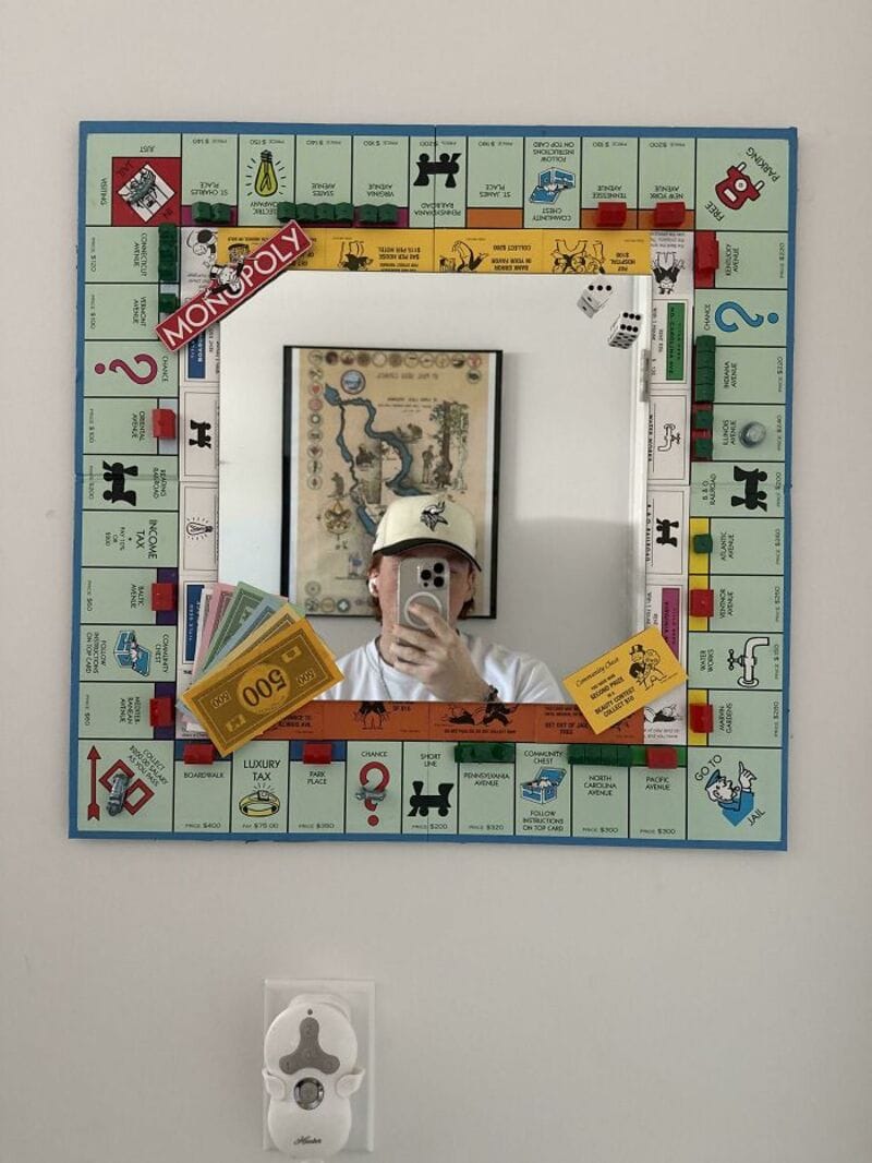 Person taking a mirror selfie with Monopoly game pieces and money in front of a mirror.