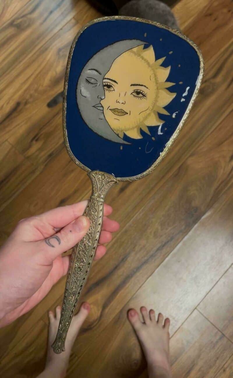 Decorative hand mirror with sun and moon design, held by a person.