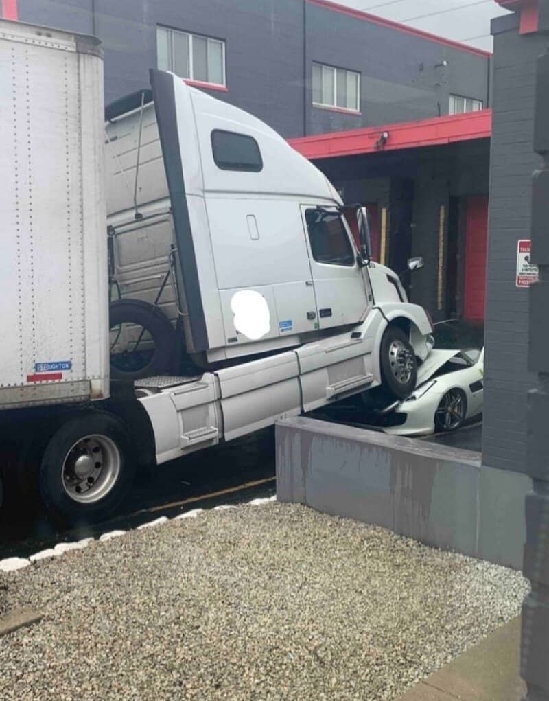 Semi-truck crashed into a building, crushing a car underneath in an urban area.