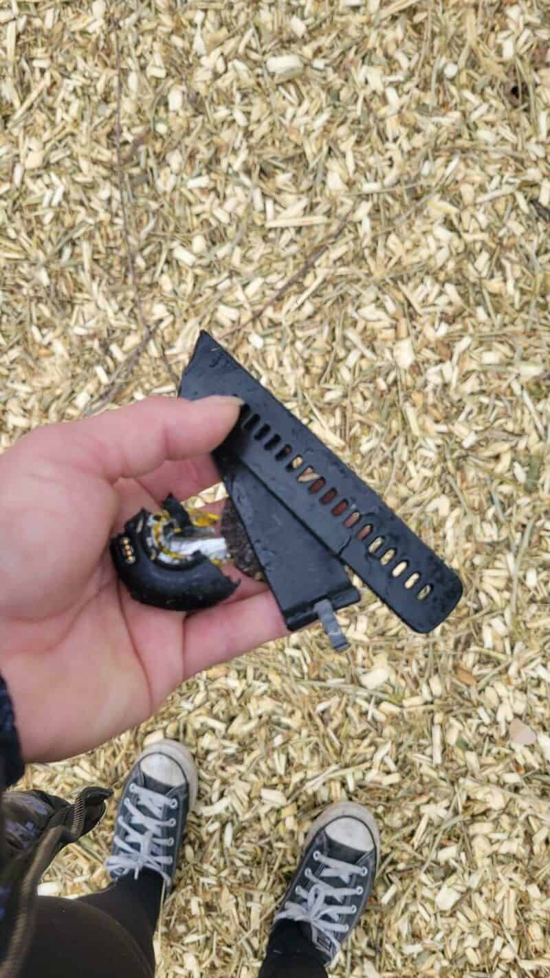 Person holding a broken black plastic object with a yellow and black component, on wood chips.