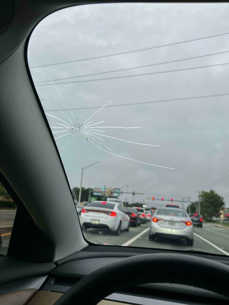 Windshield with cracked glass on a busy road with cars and traffic lights.