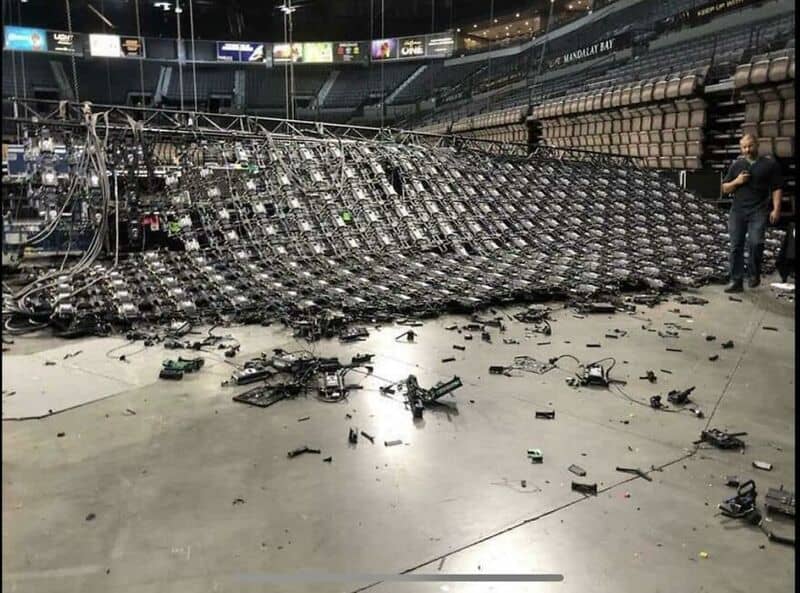 Large collapsed lighting rig with scattered debris in an arena.