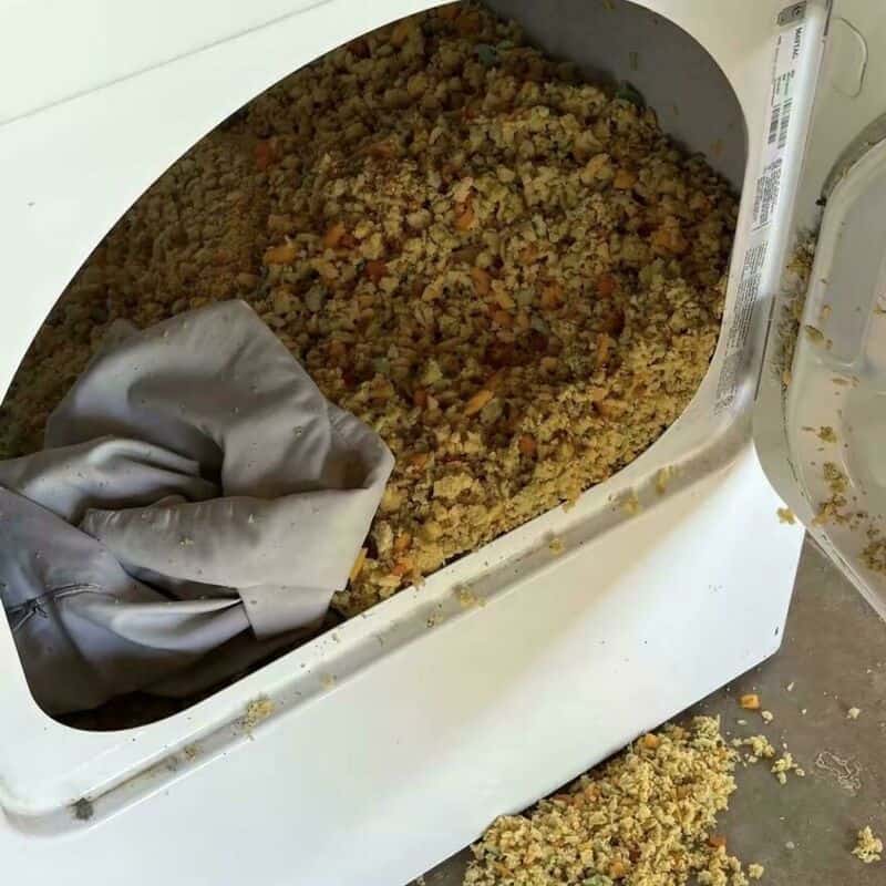 Washing machine filled with a large amount of bread crumbs and a gray cloth inside.