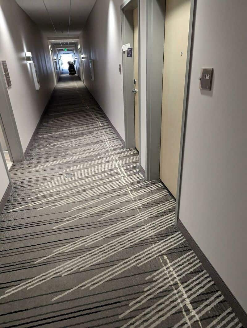 Empty hotel corridor with patterned carpet and closed doors on both sides.