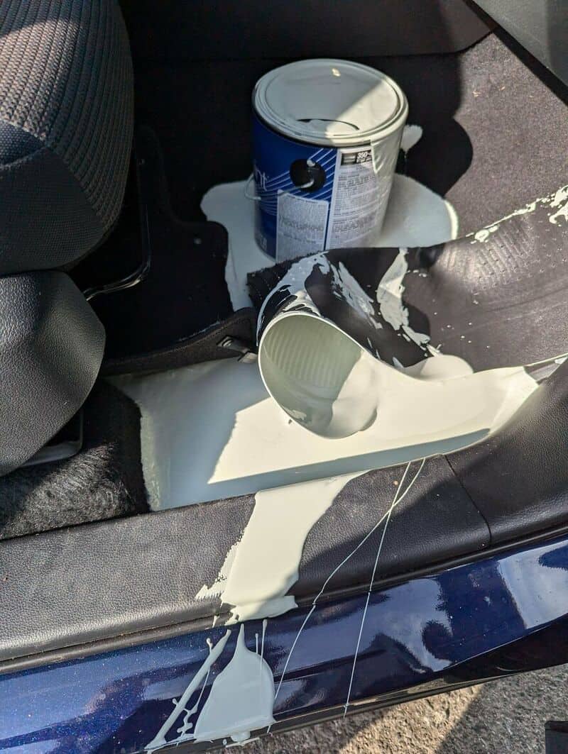 Paint spilled inside car, with a paint can and spilled paint on the floor and seat.