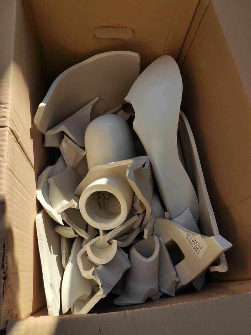 Disassembled white plastic parts in a cardboard box.