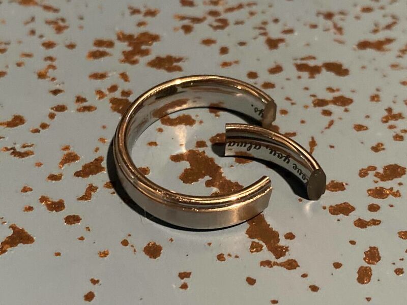 A gold-colored ring with a black and white inscription on a speckled surface.