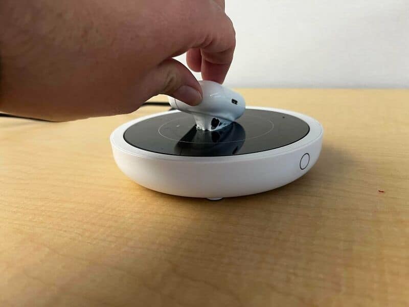 Person placing wireless earbuds on a charging dock on a wooden surface.