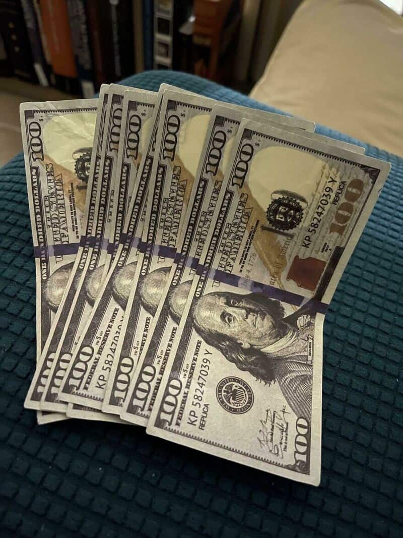 Stack of ten $100 bills on a blue textured surface.