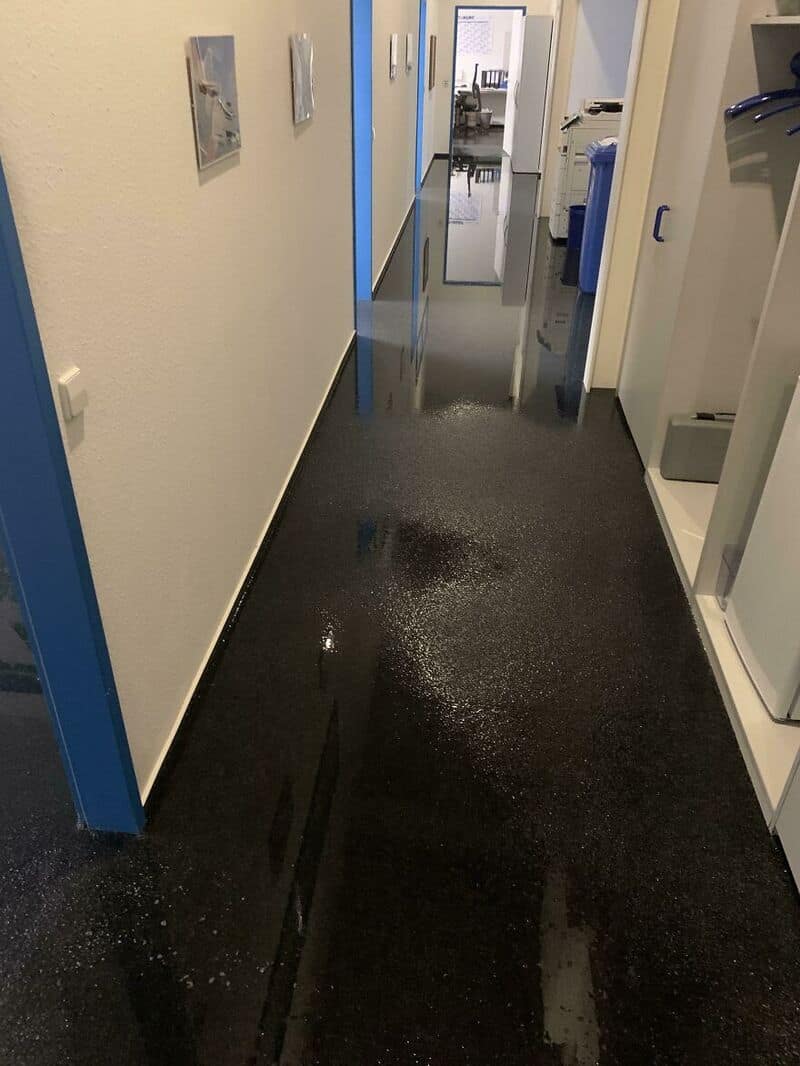 Office hallway with water on the floor, reflecting the walls and ceiling.