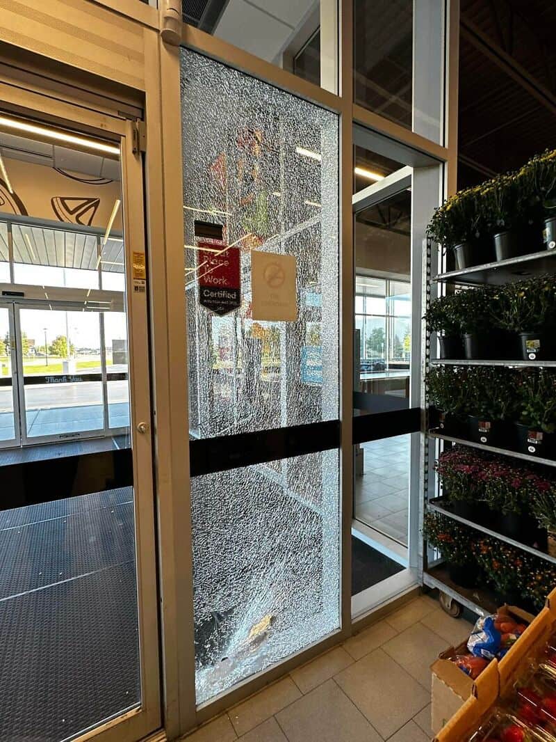 Broken glass door with water damage and signs on it at a store entrance.