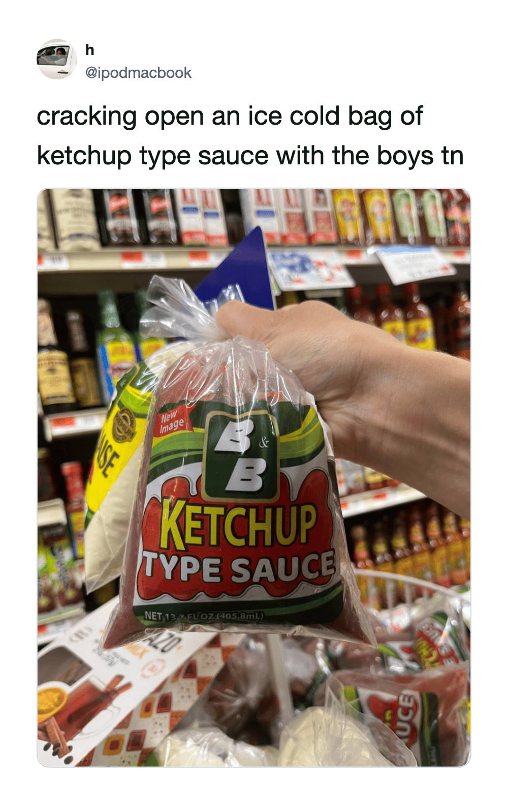 Hand holding a bag of ketchup type sauce in a grocery store aisle.