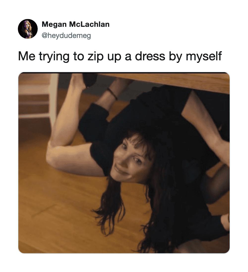 Woman trying to zip up a dress by herself, under a table.