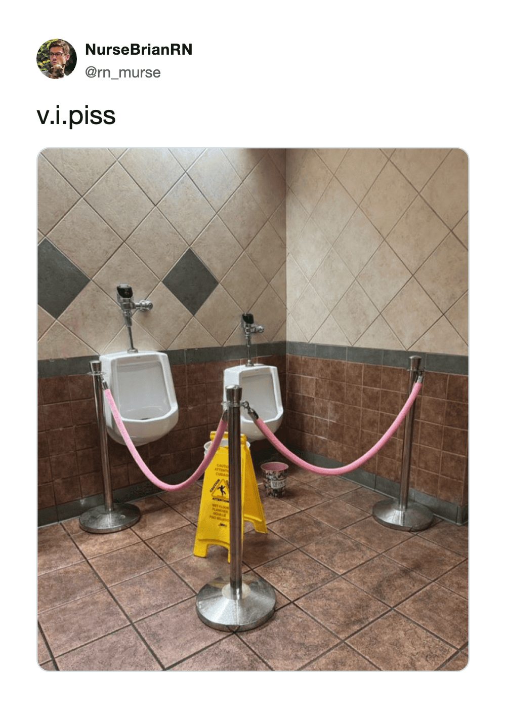 Two urinals separated by pink ropes and a yellow caution sign in a tiled bathroom.