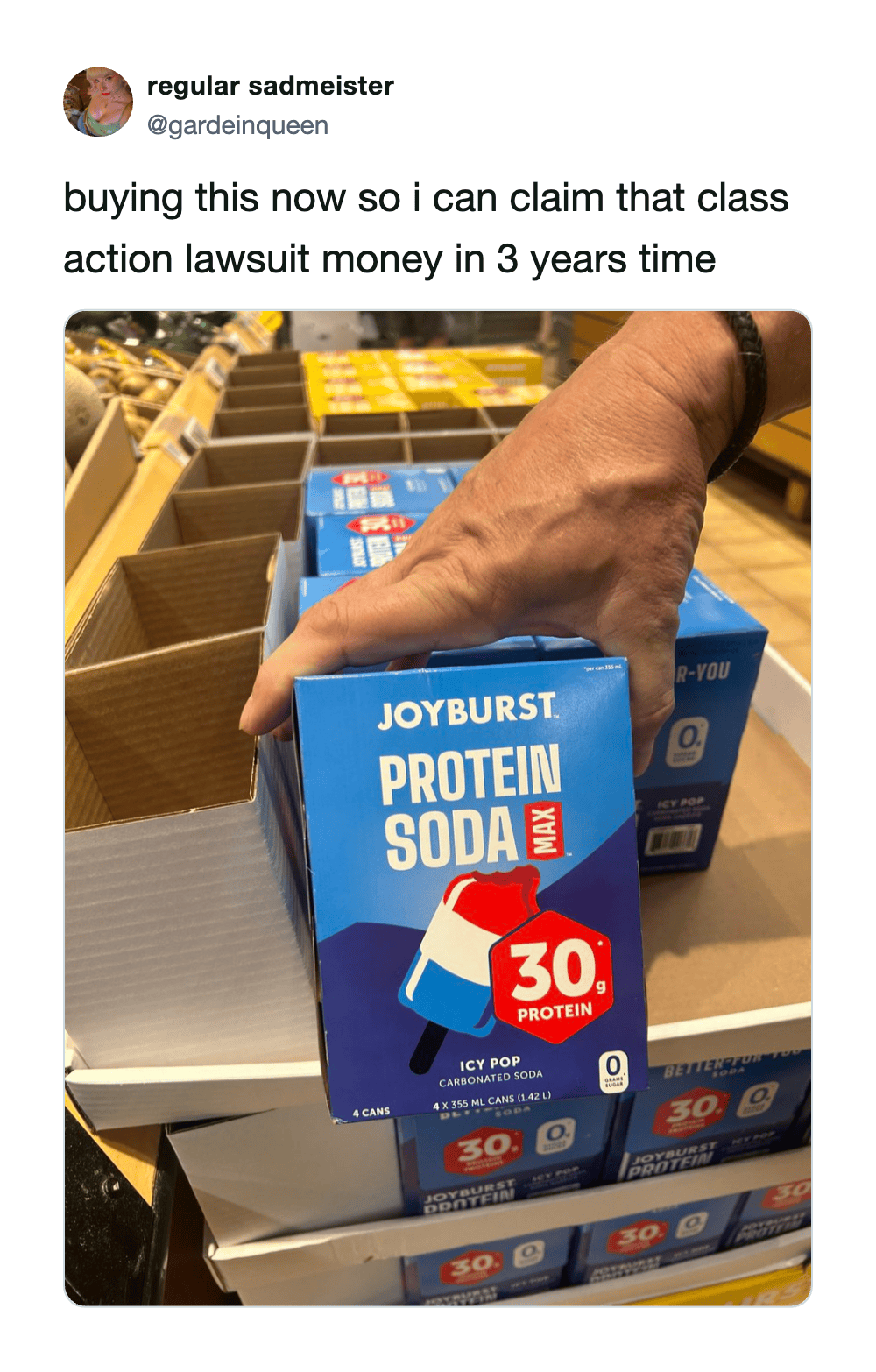 Hand holding a box of Joyburst Protein Soda in a store aisle.