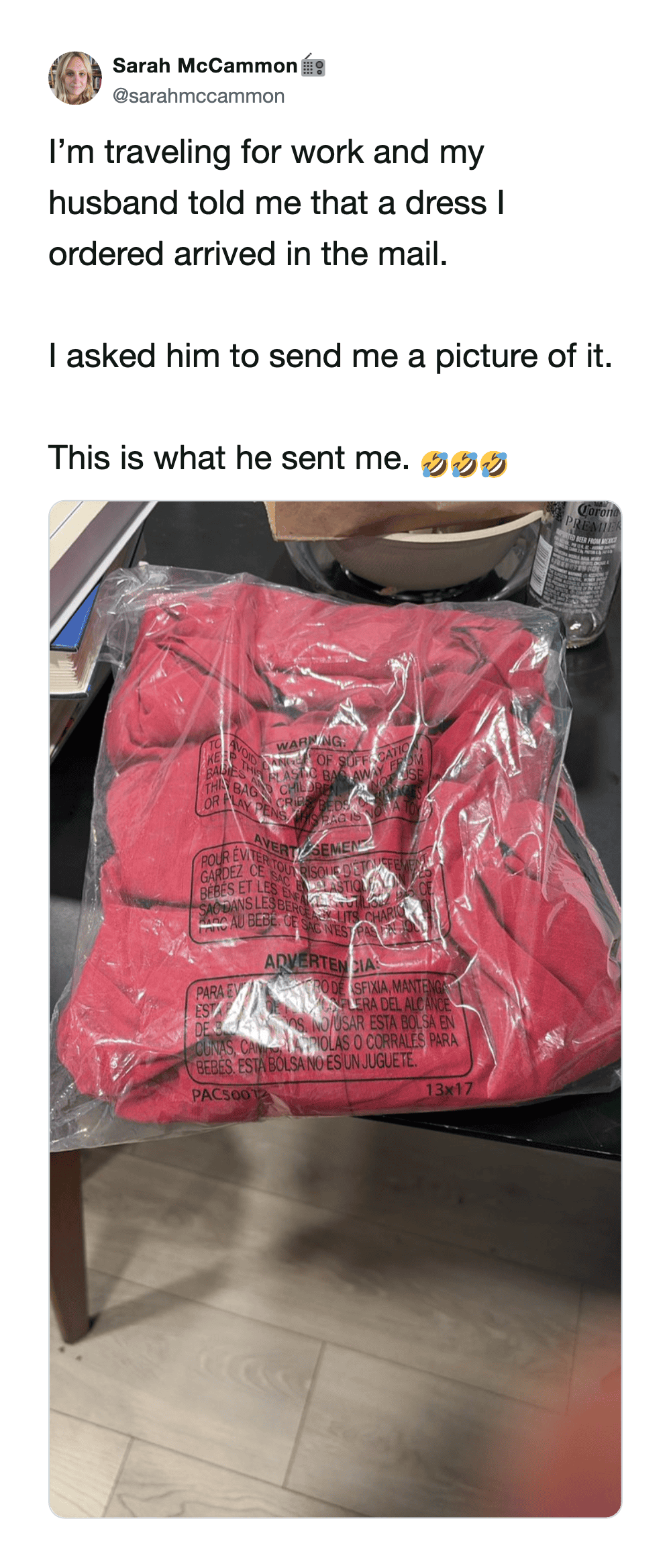 A red dress in plastic packaging on a table, with a tweet about receiving it in the mail.