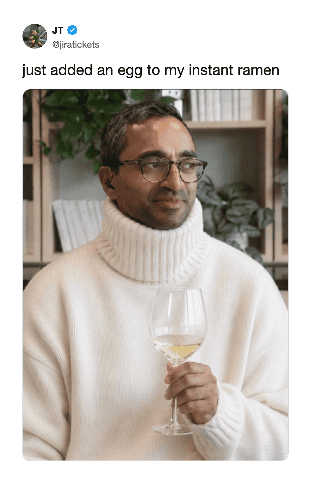 Man in glasses and white turtleneck holding a glass of white wine.