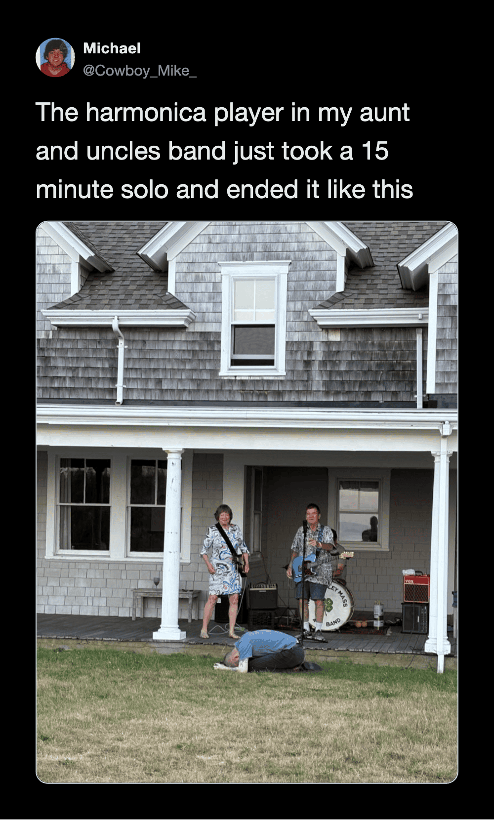 Harmonica player in front of house, band member on porch, person kneeling on grass.