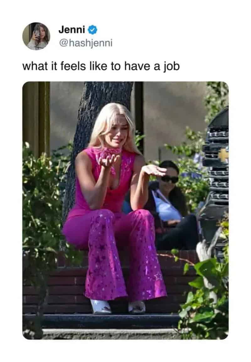 Woman in pink outfit sitting on park bench, smiling, with a hand raised.