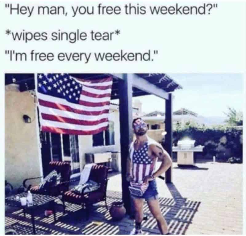 Man with American flag shorts and beard standing outside near American flag.