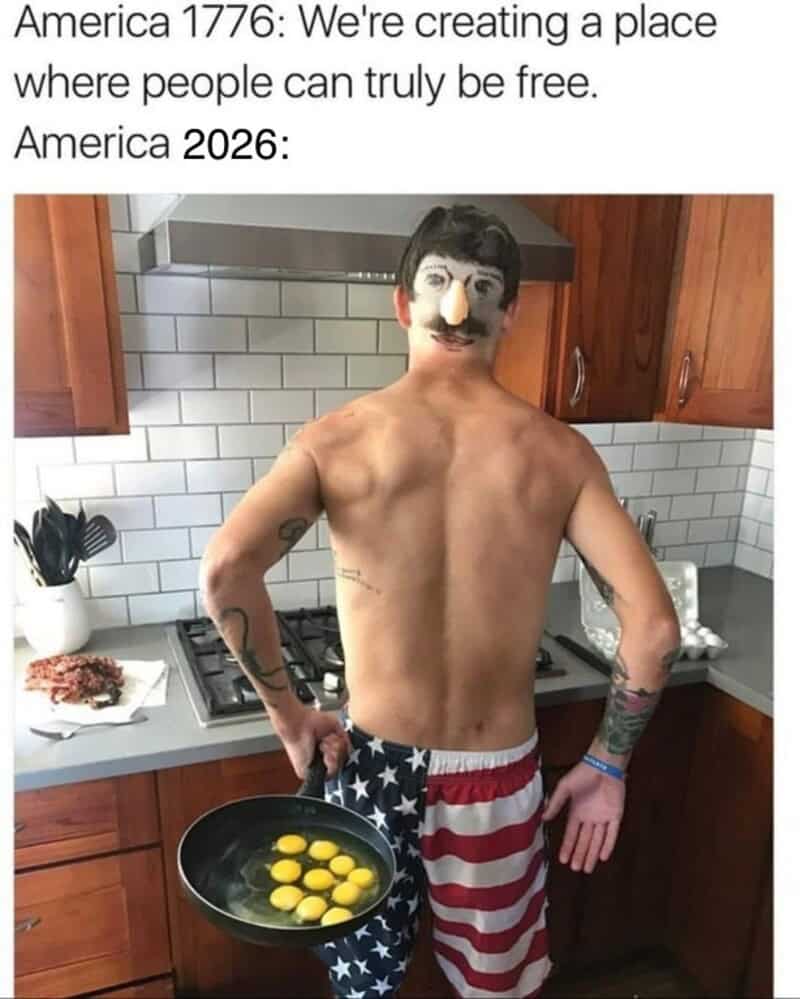 A shirtless man with a fake mustache and American flag shorts holding a frying pan with eggs.