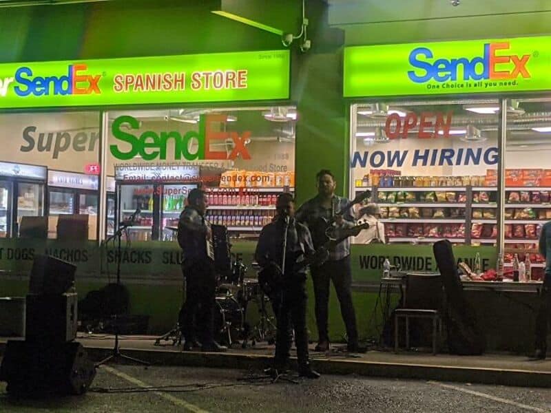 Band performing outside SendEx Spanish Store with store signs in background.