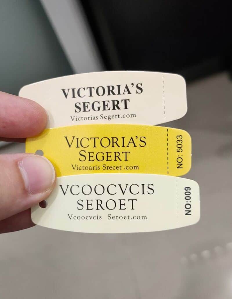 Three clothing tags with misspelled brand names, one white, one yellow, one white.
