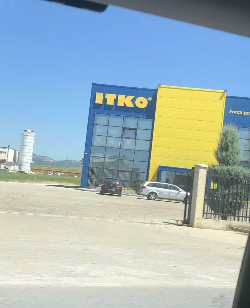 ITKO store with yellow and blue facade, cars parked outside, and a gate.