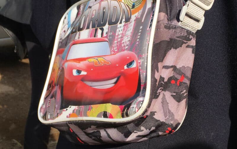 Car character from Cars movie on a backpack with city background.