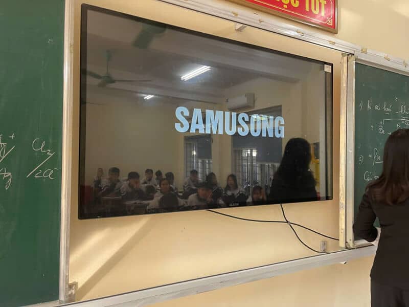 Fake Samsung logo on a classroom screen with students and teacher reflected.