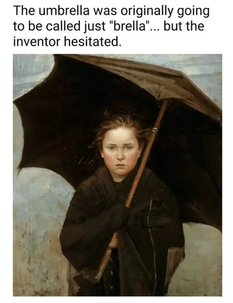 Young boy holding a large black umbrella, wearing a dark coat, with a serious expression.
