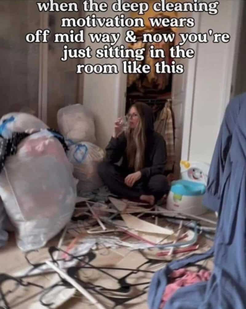 Person sitting on the floor in a messy room with cleaning supplies and clutter.