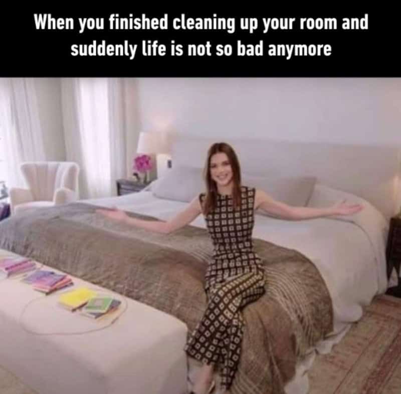 Woman sitting on bed with arms outstretched, smiling, in a hotel room.