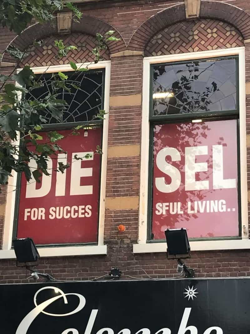 Broken window with signs reading 'DIE FOR SUCCESS' and 'SELLFUL LIVING...'.