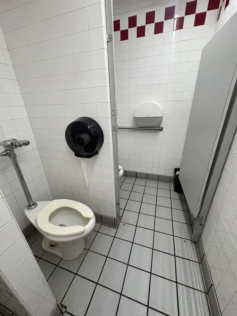 Unconventional bathroom with a toilet, paper dispenser, and a large gray cabinet.