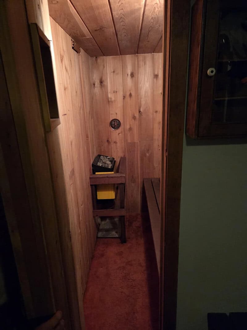 A small, narrow wooden sauna with a bench and a thermometer on the wall.