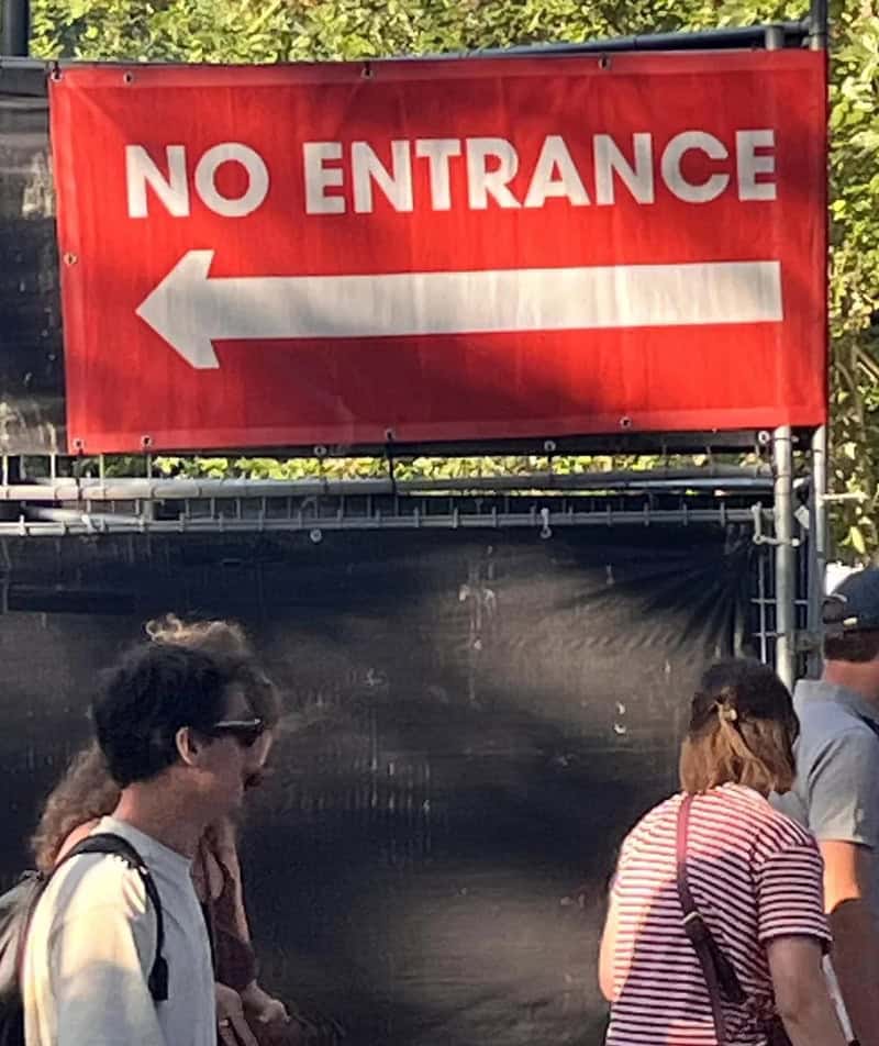 No entrance sign with a left arrow, people walking past it.