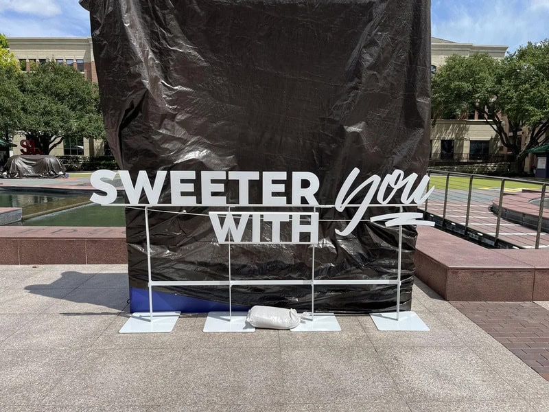 Sign reads 'SWEETER YOU WITH' with a black background and white text, partially obscured.
