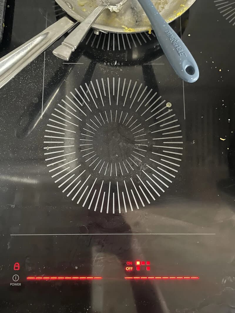 Induction cooktop with a circular pattern and cooking utensils, power indicator lights on.