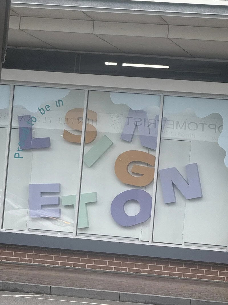 Large colorful 3D letters spelling 'PLASTIC' on a window with a reflection of the street.