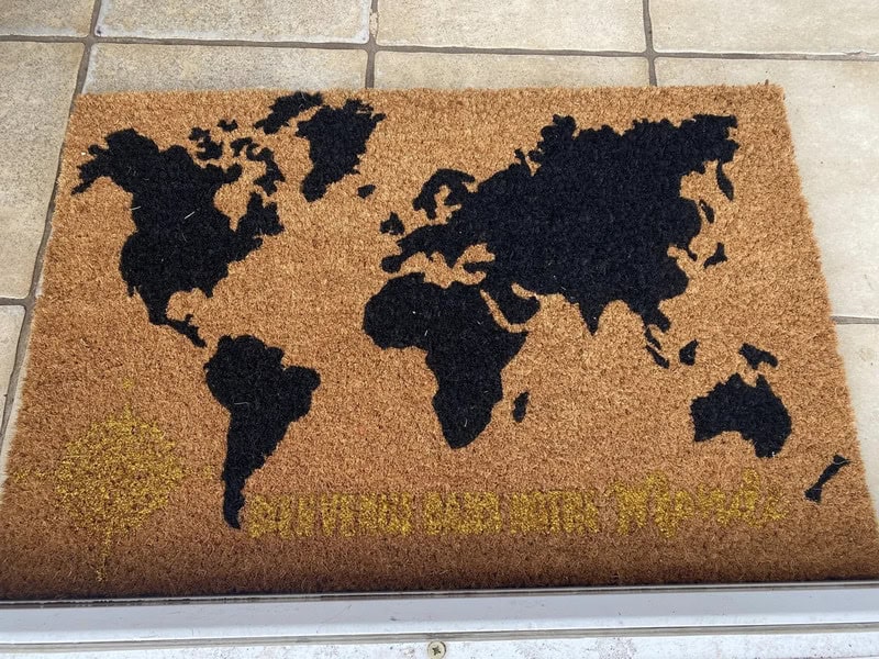 World map doormat with black continents and yellow text at the bottom.