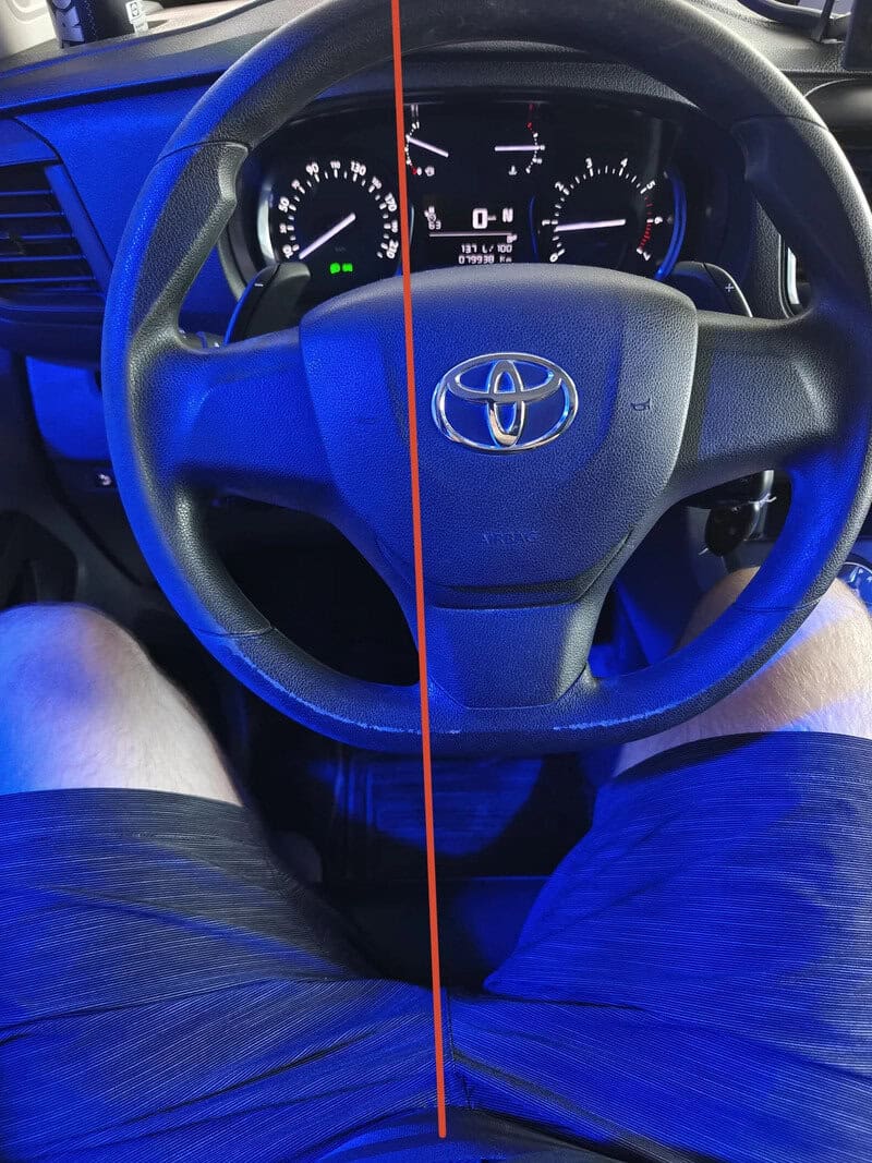 Toyota steering wheel with dashboard and legs visible, split by a red line.