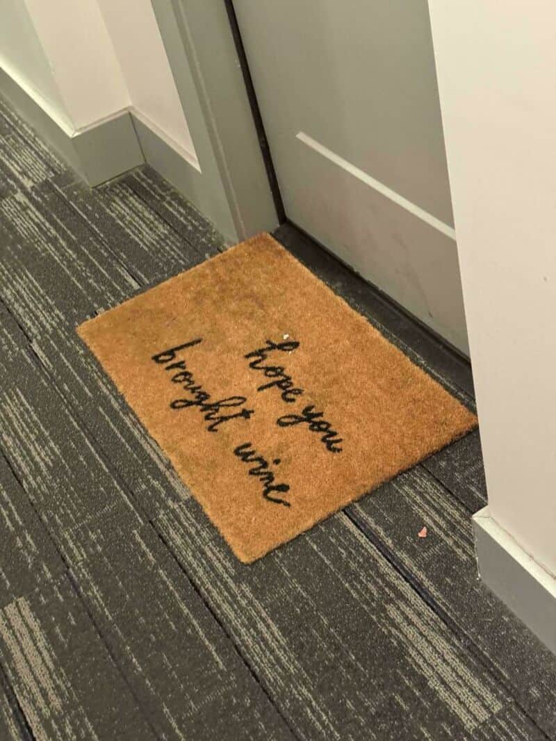 Doormat with 'hope you bought wine' text in front of a door.