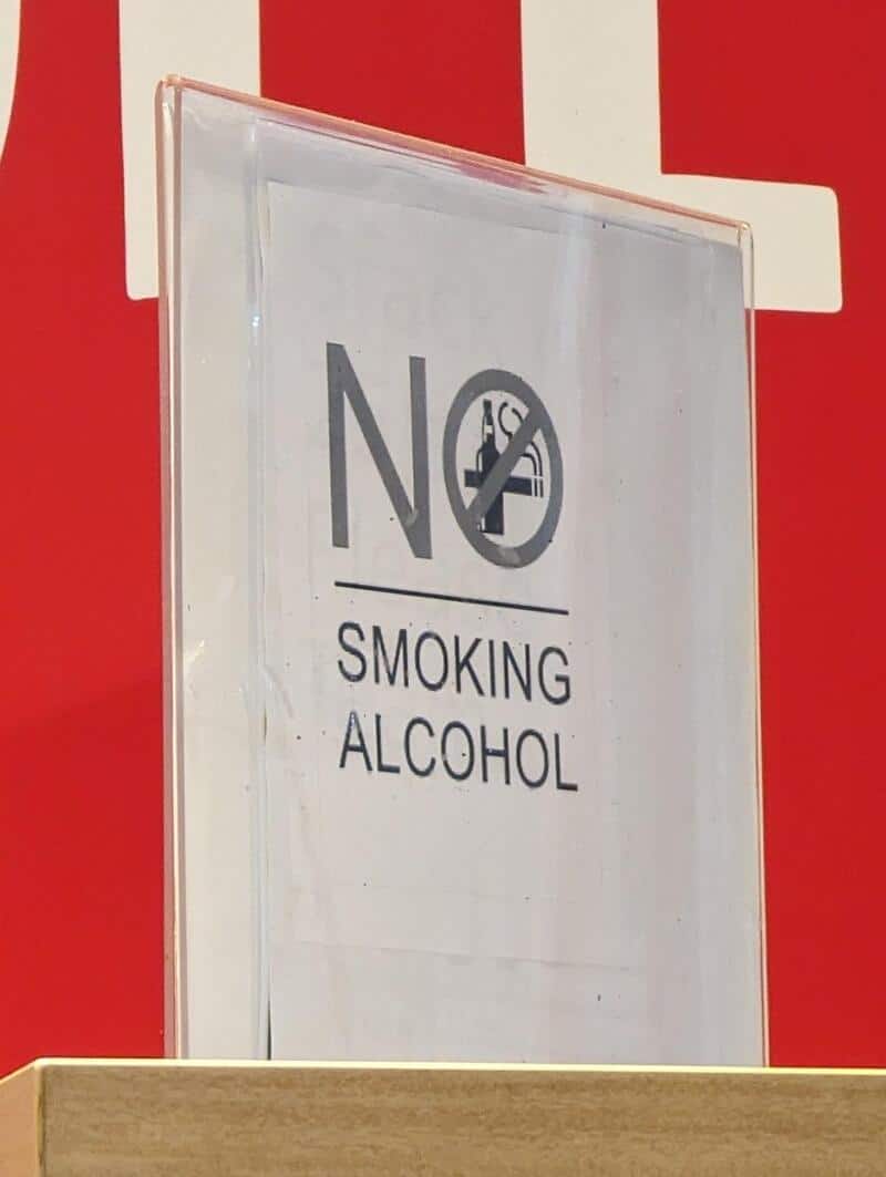 No smoking or alcohol sign on a clear stand against a red background.