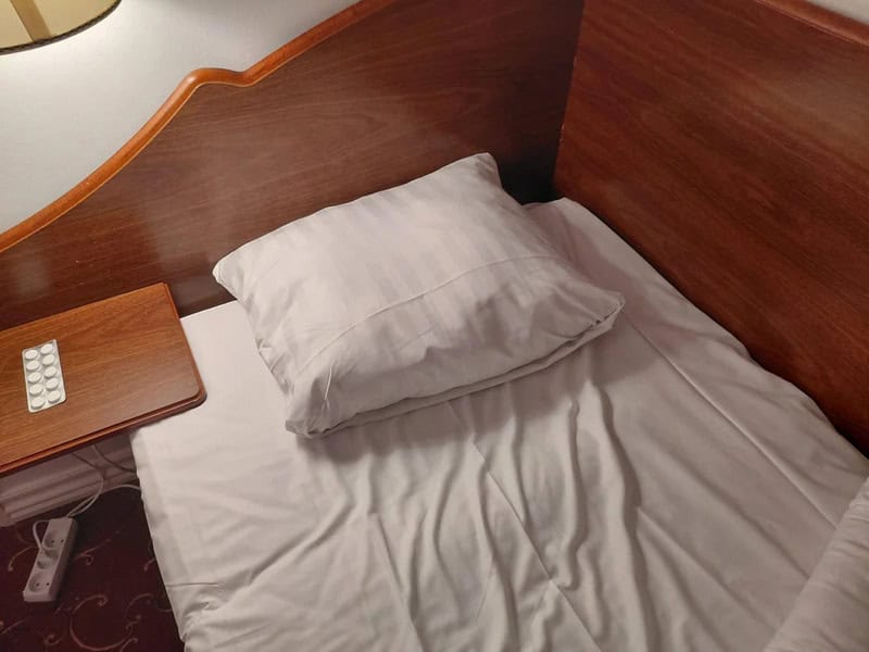 Messy bed with a pillow and a wooden headboard in a hotel room.