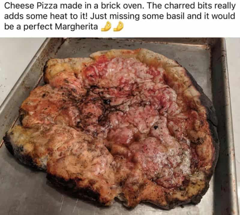 Cheese pizza with charred bits, missing basil, on a baking sheet.